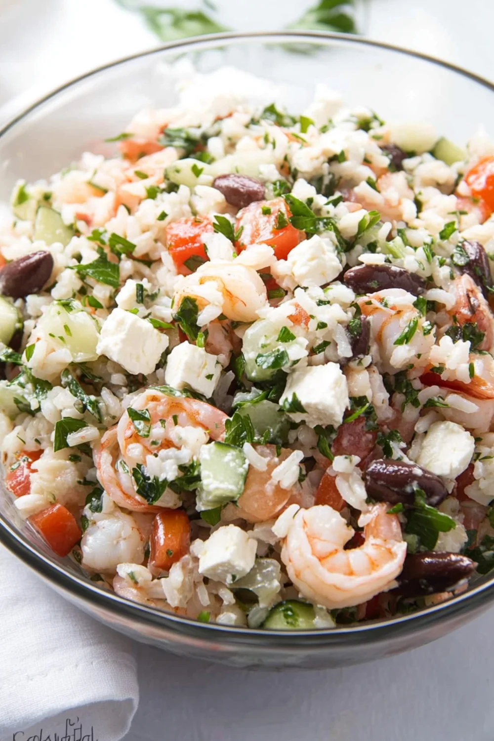 A vibrant bowl of Greek Shrimp Salad with feta cheese, rice, black beans, cucumbers, tomatoes, and fresh parsley.