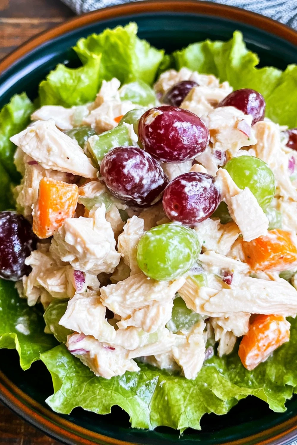 A fresh serving of Chicken Salad with Grapes, featuring tender shredded chicken mixed with green and red grapes, celery, and carrots, all resting on a bed of crisp lettuce.