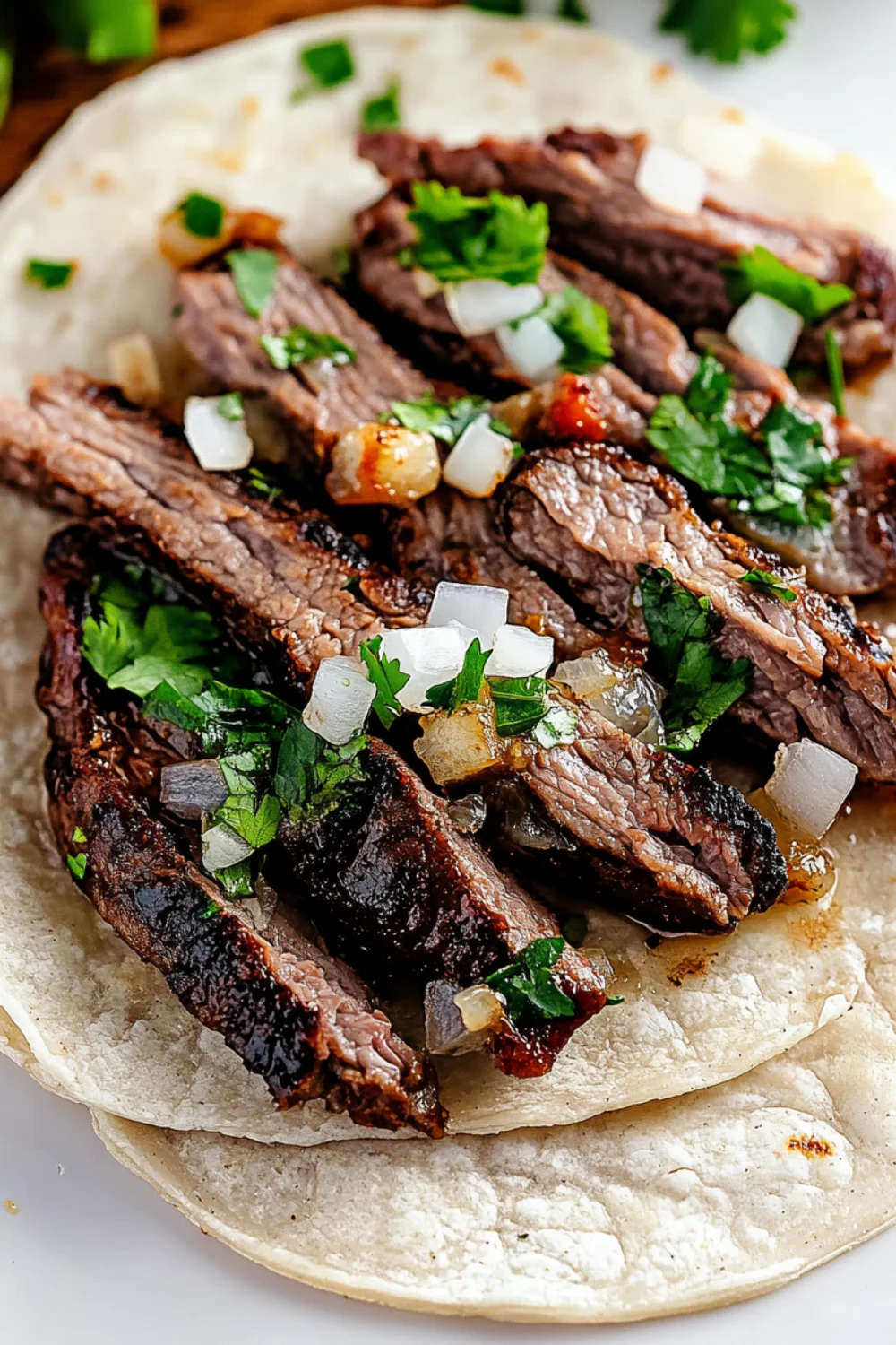 A close-up of a warm tortilla filled with juicy slices of grilled carne asada, topped with fresh cilantro and diced onions.