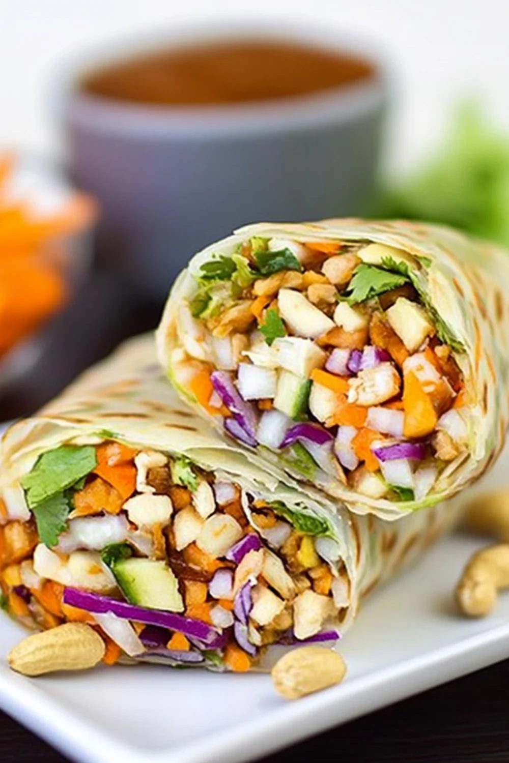 A delicious Thai Peanut Wrap filled with fresh veggies like carrots, cucumber, red cabbage, cilantro, and peanuts, wrapped in a soft tortilla with a side of dipping sauce.