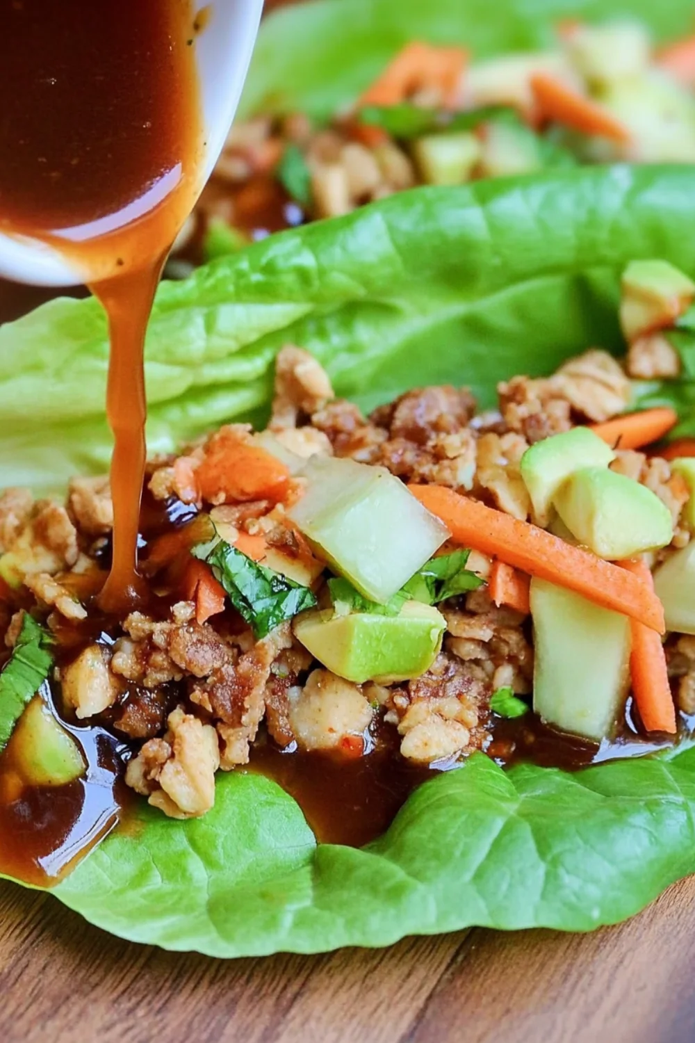 A close-up of Vegetarian Lettuce Wraps filled with savory seasoned vegetables, topped with fresh carrots, cucumbers, and avocado slices, and drizzled with a flavorful sauce, all inside a crisp green lettuce leaf.