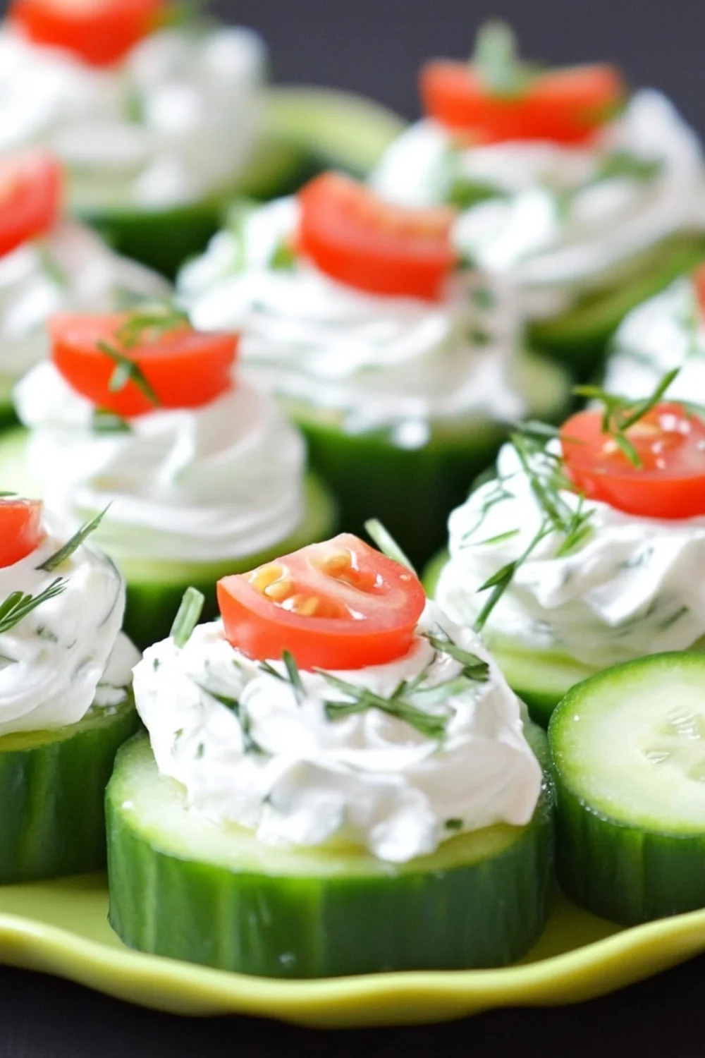 Fresh cucumber rounds topped with creamy dill cheese spread and garnished with cherry tomato halves and fresh herbs.
